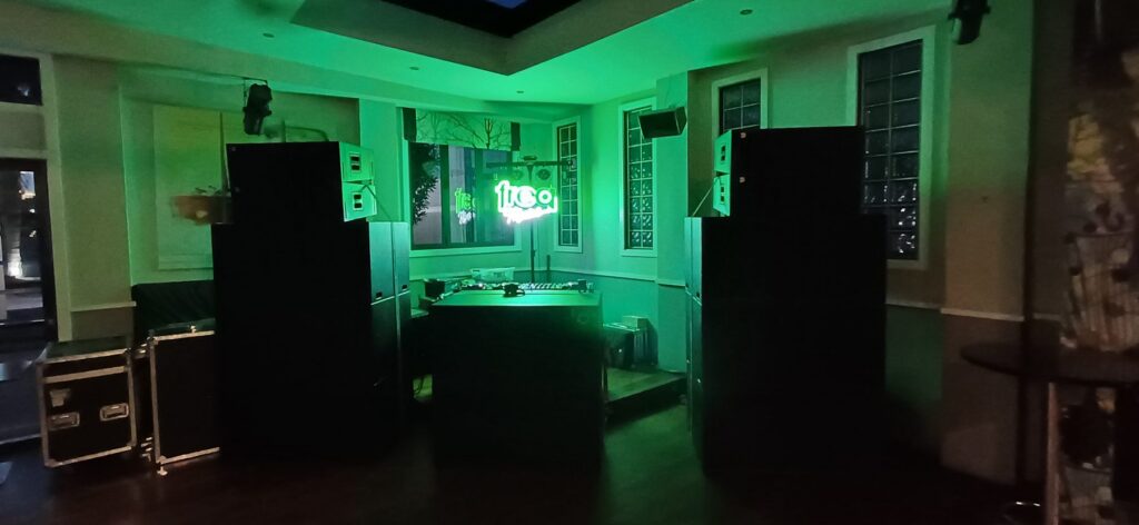 DJ booth and PA speakers lit in green in a venue