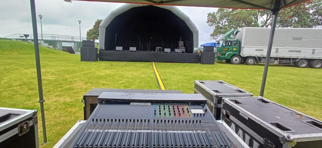 Front-of-house mixing desk looking towards an inflatable stage cover at an outdoor event