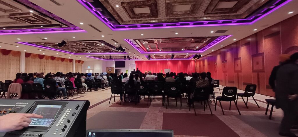 Function room with purple and pink uplighting, banquet seating and a presentation screen