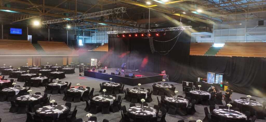 Gala dinner with round banquet tables facing a stage lit in red