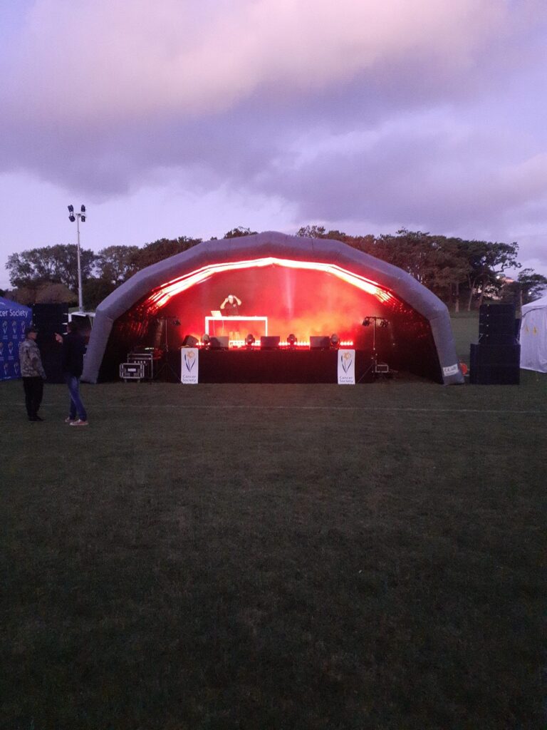 Inflatable stage cover lit in red at dusk at an outdoor event
