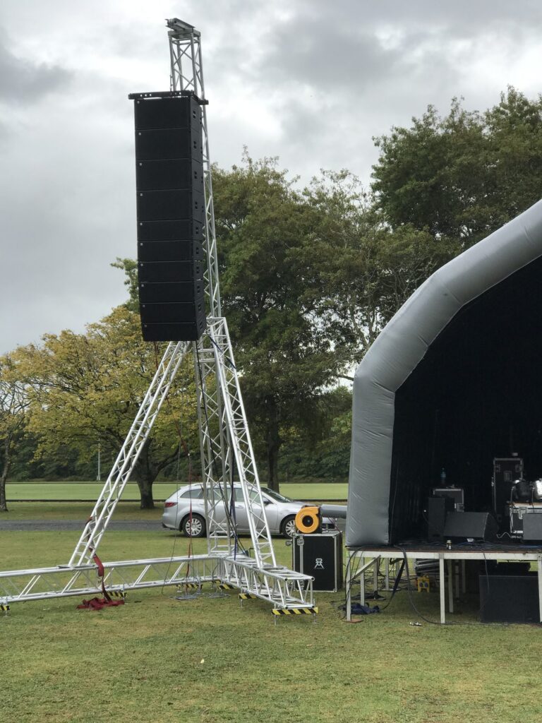 Line array PA speakers on a ground-stacked tower beside an inflatable stage