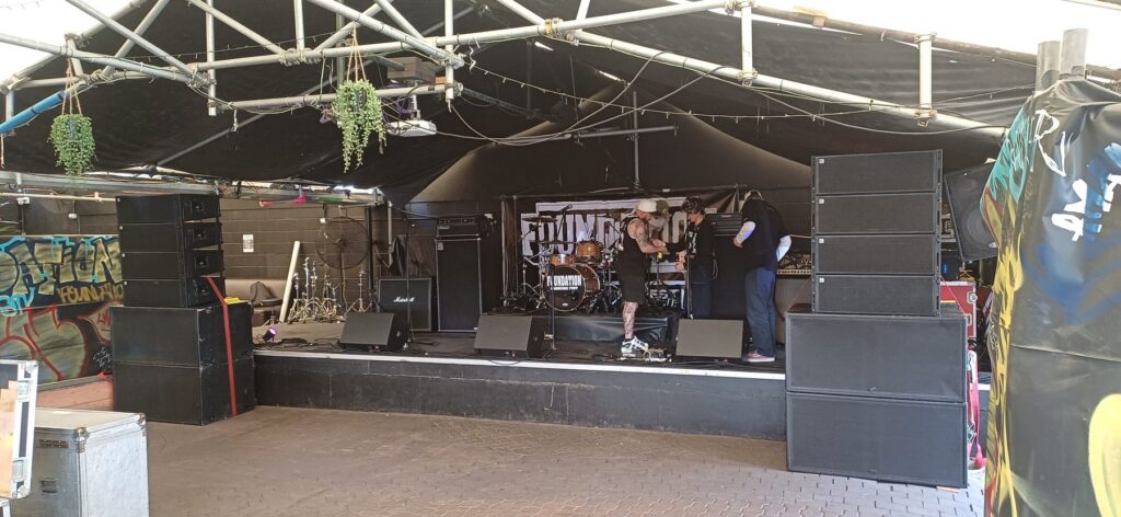 Band setting up on stage between large line array PA stacks at a live music venue